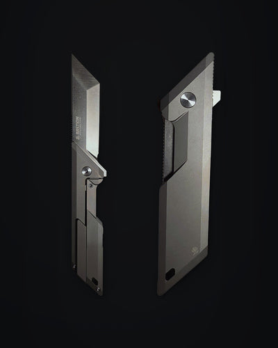 Two views of a sleek, minimalist folding utility knife in a matte dark gray finish, displayed against a solid black background. Bastion Legend Glassbead finish.