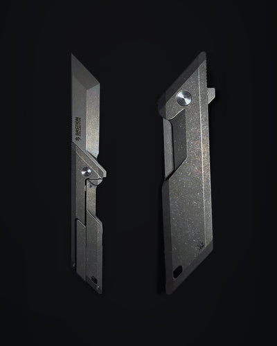 Two views of a dark gray tactical utility knife blade set against a solid black background, showing both the open blade profile and the closed handle profile.